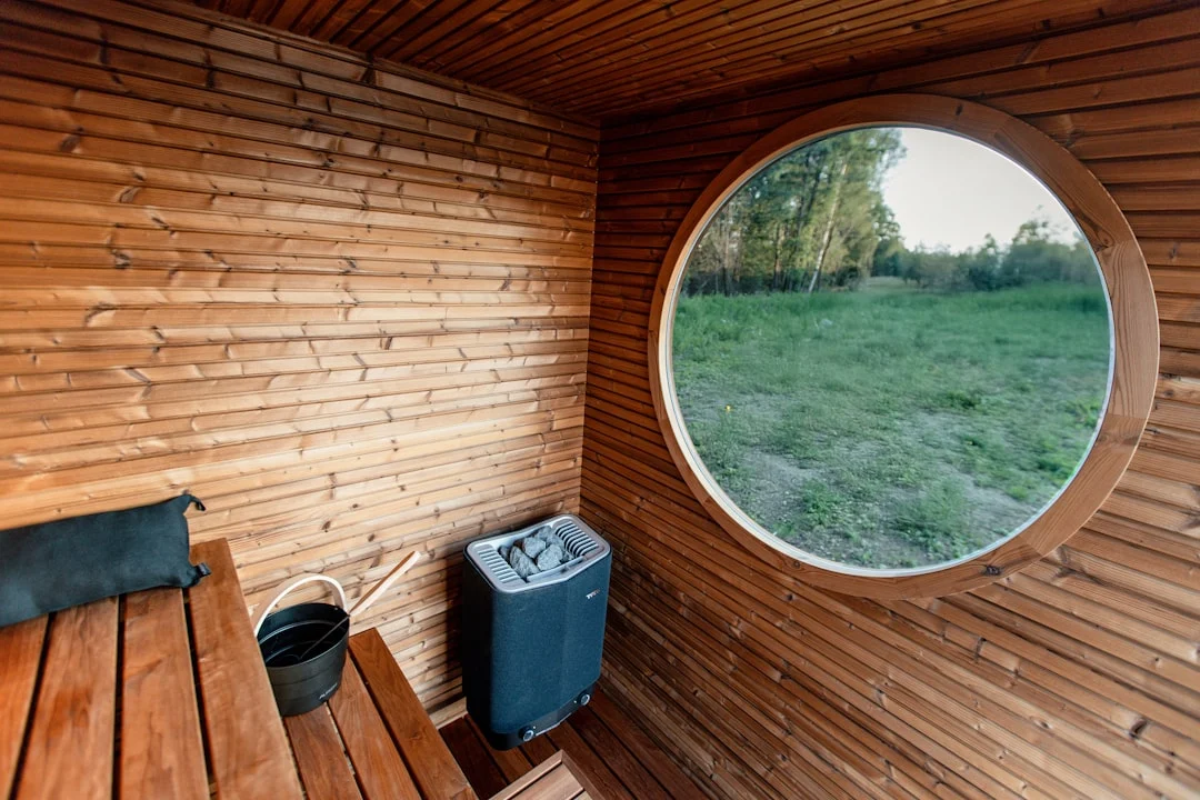 Moderni saunan sisätila puupaneelein, lautein ja pyöreällä panoraamaikkunalla – näkymä metsään.